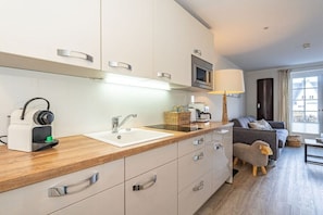 A modern kitchen with a wooden countertop, a built-in microwave, and a sink. There is a sofa and a lamp in the adjacent living area. - Holiday apartment with 1 bedroom (Rantum, Sylt)