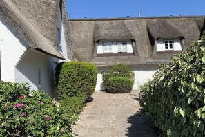 A traditional thatched-roof house with a narrow stone pathway leading to the entrance. - Holiday apartment with 1 bedroom (Rantum, Sylt)
