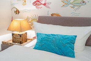 A bed with a white pillow and a teal pillow, a wooden bedside table with a lamp, and a wall with fish decals. - Holiday apartment with 1 bedroom (Rantum, Sylt)