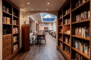 Una biblioteca con estanterías a ambos lados, un área central de estar con mesas y sillas, y un techo con tragaluces.