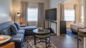 A modern hotel room with a sofa, a small round table, a flat-screen TV, and a bed. - Downtown Views | Pet-friendly & In-Room Dining (Portland)