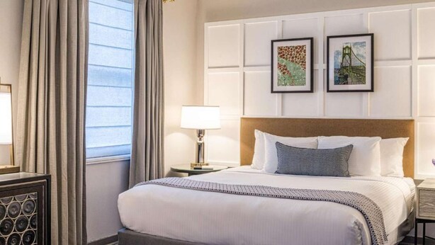 A hotel room with a bed, a nightstand, a lamp, and two framed pictures on the wall. - Downtown Views | Pet-friendly & In-Room Dining (Portland)