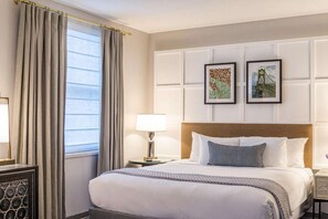 A hotel room with a bed, a nightstand, a lamp, and two framed pictures on the wall. - Downtown Views | Pet-friendly & In-Room Dining (Portland)
