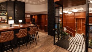 A bar area with stools, a bar counter, and a view of a staircase leading to a lower level. - Downtown Views | Pet-friendly & In-Room Dining (Portland)