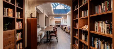 A library with bookshelves on both sides, a central seating area with tables and chairs, and a skylight ceiling.