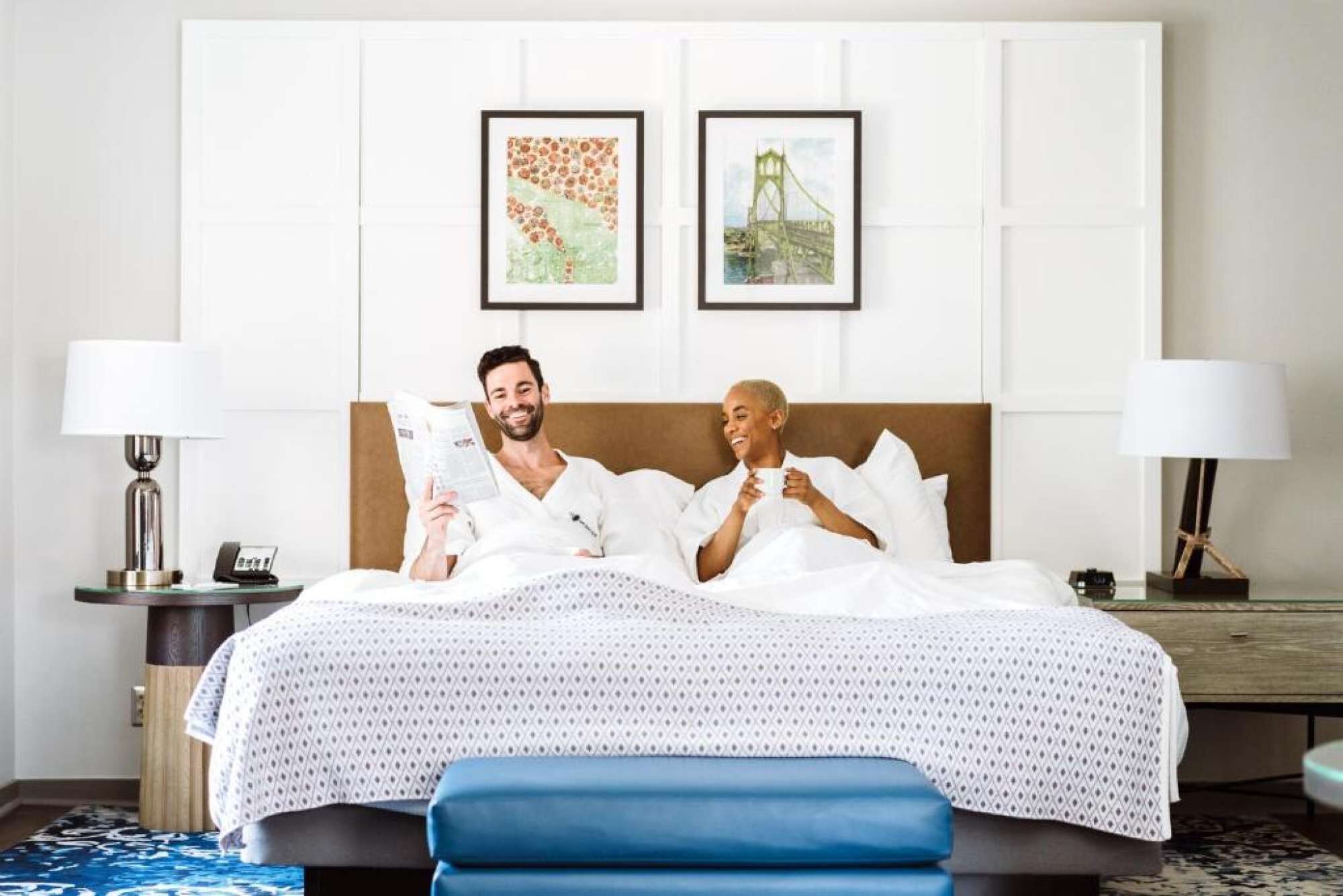 Une chambre d’hôtel avec un lit, deux lampes de chevet, une table de chevet et deux tableaux encadrés au mur.