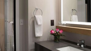 Un bany modern amb plat de dutxa de vidre, un lavabo amb mirall i un ram de flors.