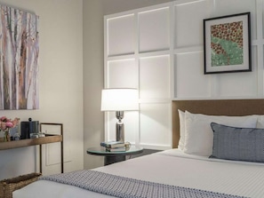 A hotel room with a large bed, a bedside table with a lamp, a framed picture on the wall, and a decorative piece above the bed. - Walk to Schnitzer & Powell’s | Bike & Pet-friendly (Portland)