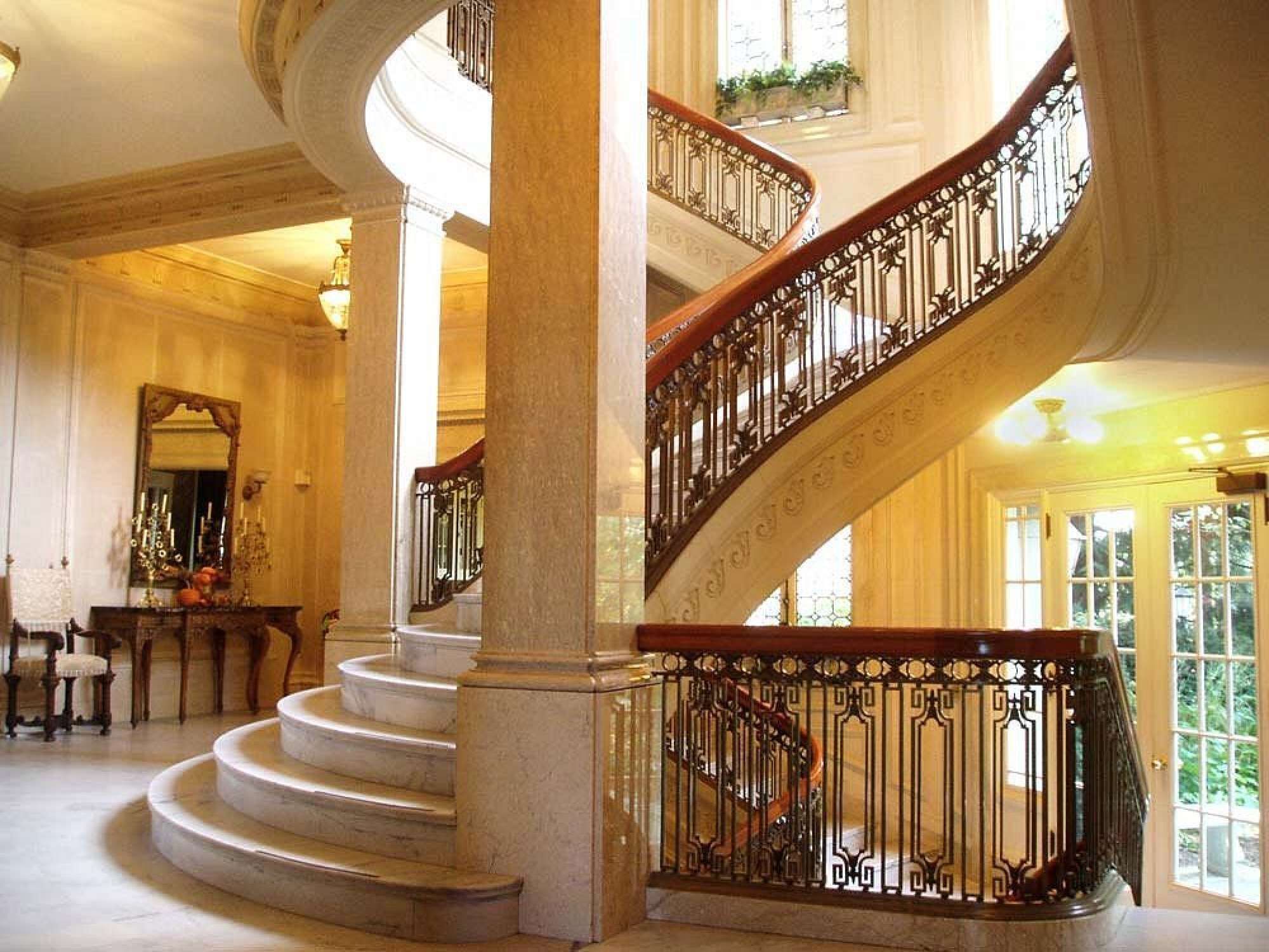 A grand spiral staircase with ornate metal railings, marble steps, and a large mirror on the wall.