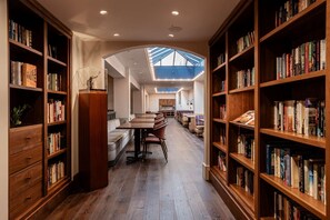 A library with bookshelves on both sides, a central seating area with tables and chairs, and a skylight ceiling. - Walk to Schnitzer & Powell’s | Bike & Pet-friendly (Portland)