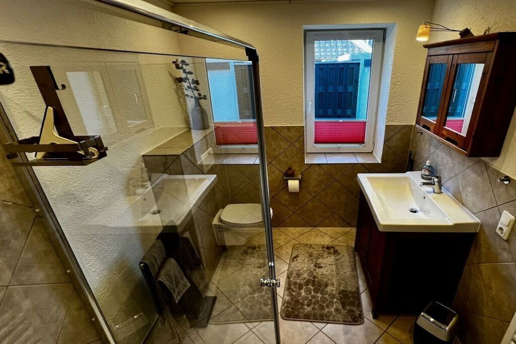 Een badkamer met een douchecabine van glas, toilet, wastafel en raam.
