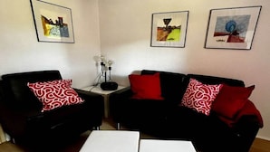 Ein Wohnzimmer mit zwei schwarzen Sofas, jedes mit einem roten und weißen Kissen, einem weißen Couchtisch und drei gerahmten Kunstwerken an der Wand.