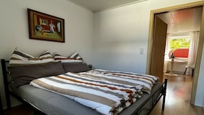 Ein Schlafzimmer mit Bett, Kissen, einem Bild an der Wand und einer Tür zu einem anderen Raum.