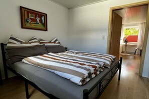 Een slaapkamer met een bed, kussens, een schilderij aan de muur en een deur naar een andere kamer.
