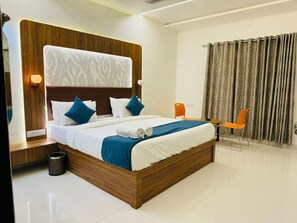 A modern hotel room with a wooden headboard, a large bed with white and blue bedding, two orange chairs, and a curtain. - Sorathgadh Resort Sasan Gir (Sasan Gir)