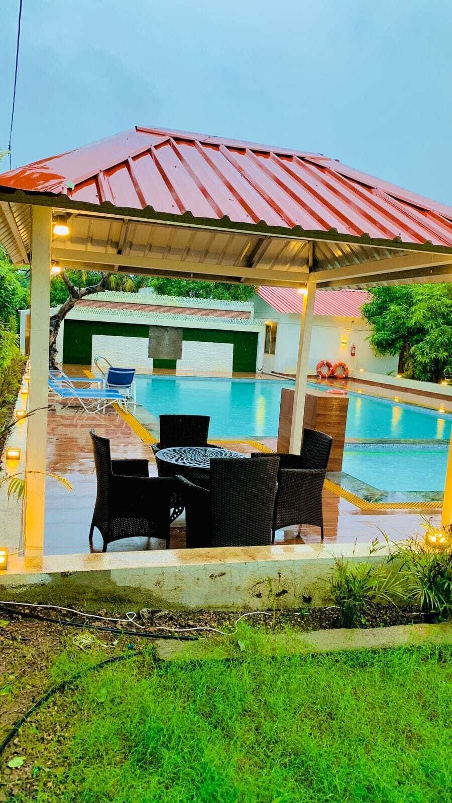 A covered outdoor seating area with a pool in the background.
