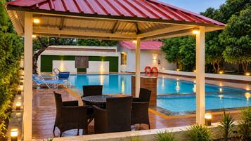 A covered outdoor area with a pool, lounge chairs, and a table.