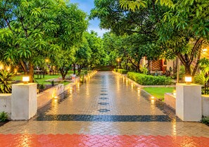 A paved pathway flanked by trees and illuminated by ground lights, leading to a building entrance.