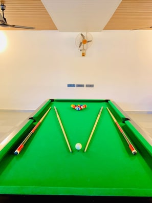 A pool table with a green felt surface, two pool cues, a cue ball, and a set of colored balls.