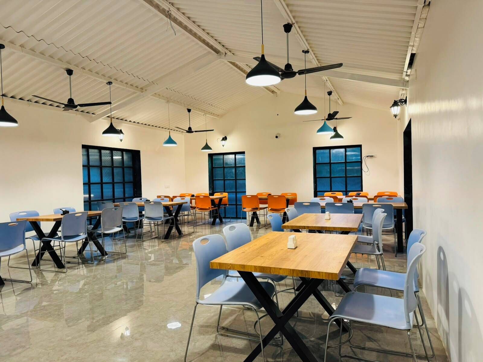Un salón de conferencias con varias mesas y sillas, ventiladores de techo e iluminación colgante.