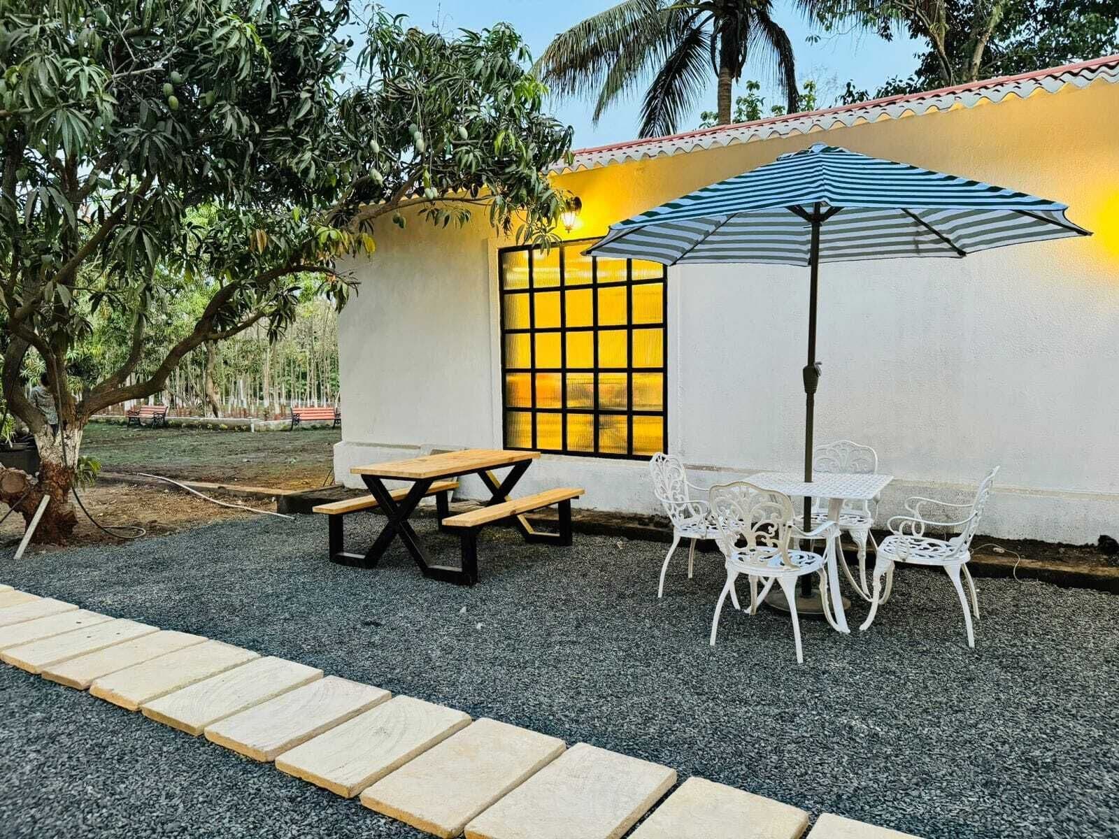 Un área de estar al aire libre con una mesa, sillas, un banco y un paraguas a rayas.