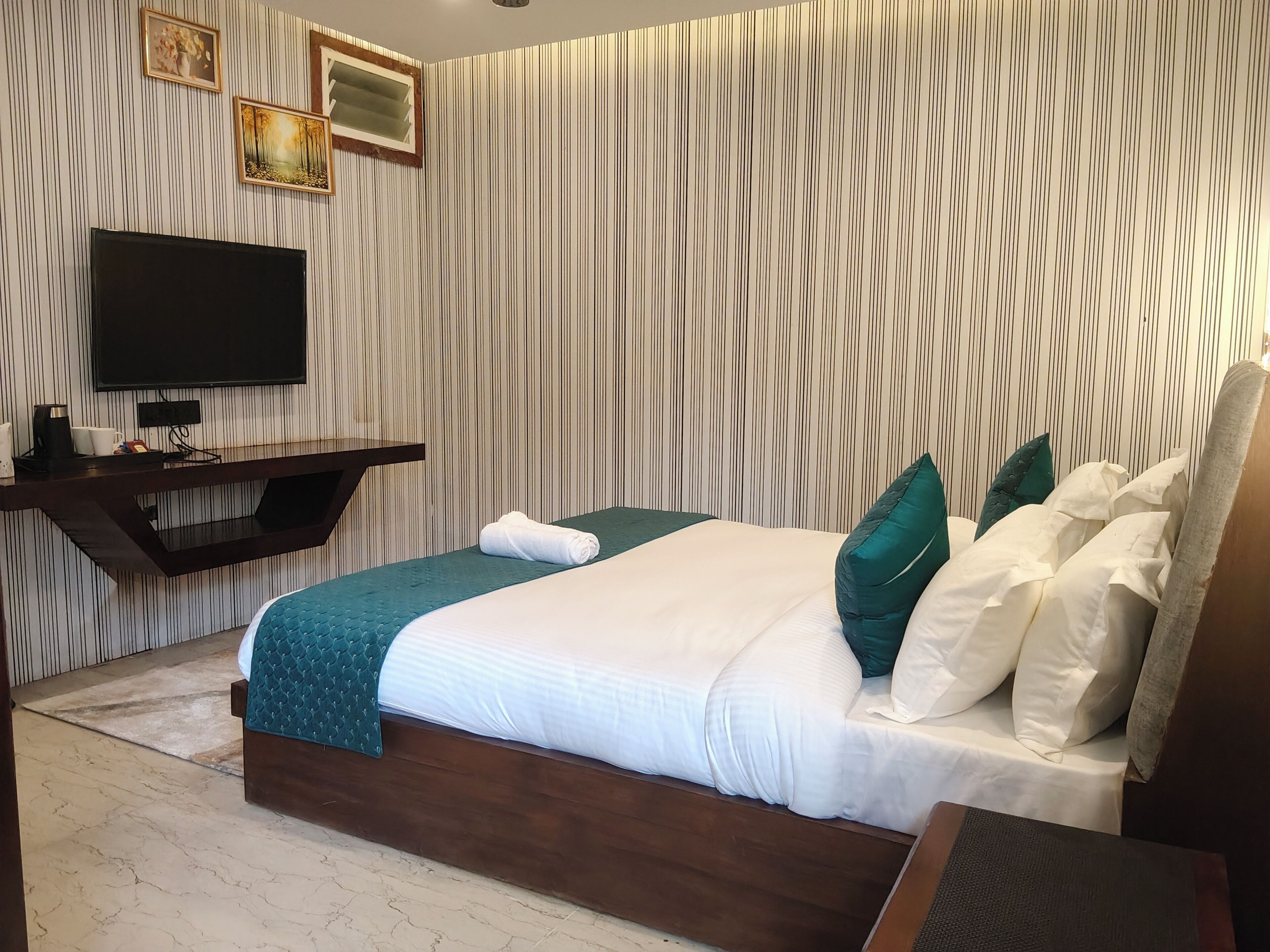 Ein Hotelzimmer mit einem Bett, einem Flachbildfernseher, einem Holznachttisch und einer Wand mit vertikalen Streifen.