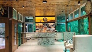 A modern interior with a wooden ceiling, a marble counter, and a view of a mountainous landscape through large windows. - Cottages & Cafe (Kotdwar)
