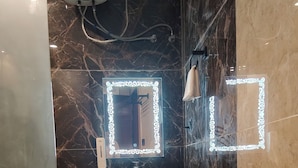 A bathroom with a white sink, a mirror with decorative lights, and a trash bin. - Cottages & Cafe (Kotdwar)