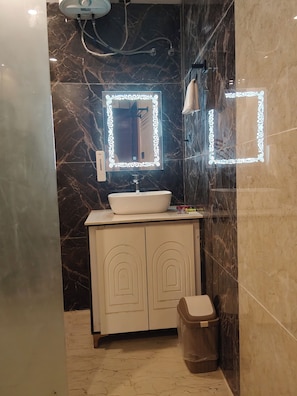 A bathroom with a white sink, a mirror with decorative lights, and a trash bin. - Cottages & Cafe (Kotdwar)