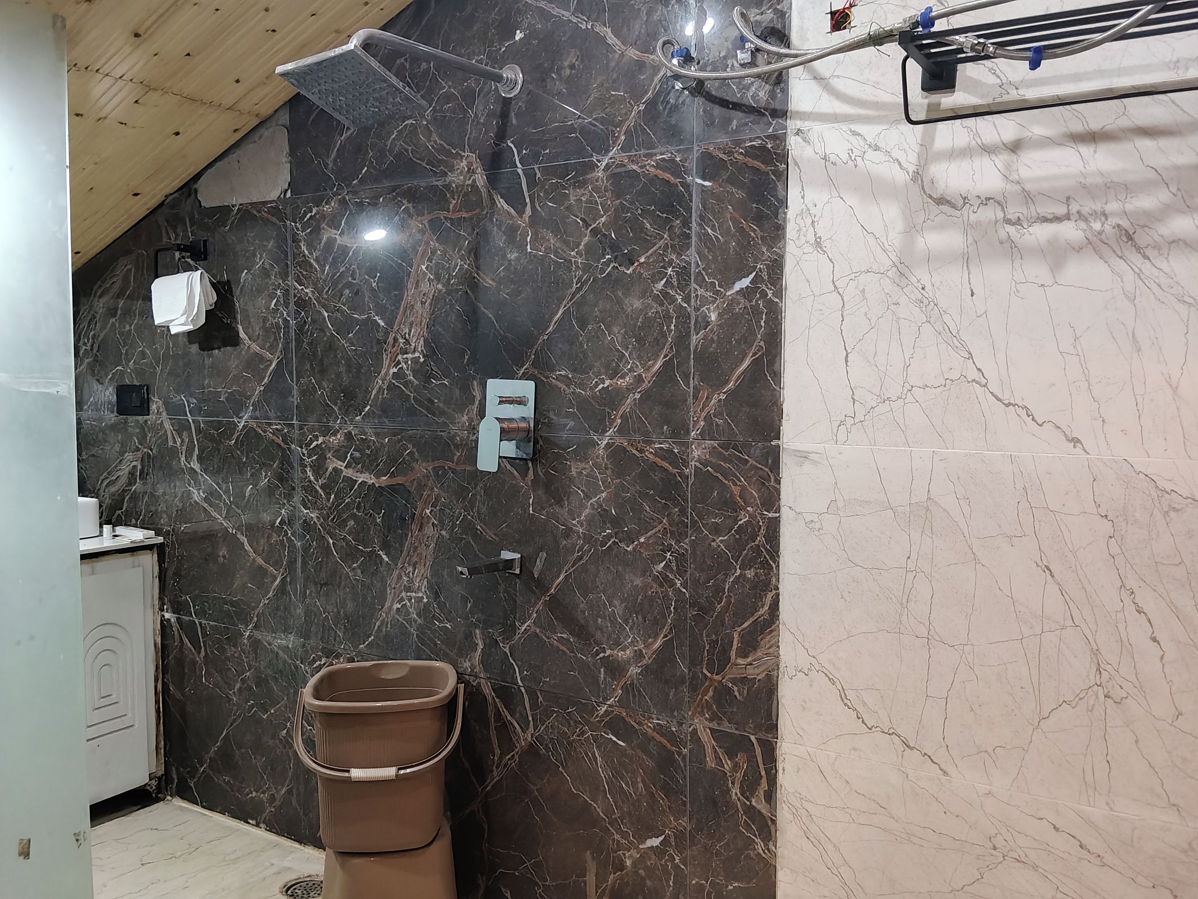A bathroom with a shower, a towel rack, and a trash bin.
