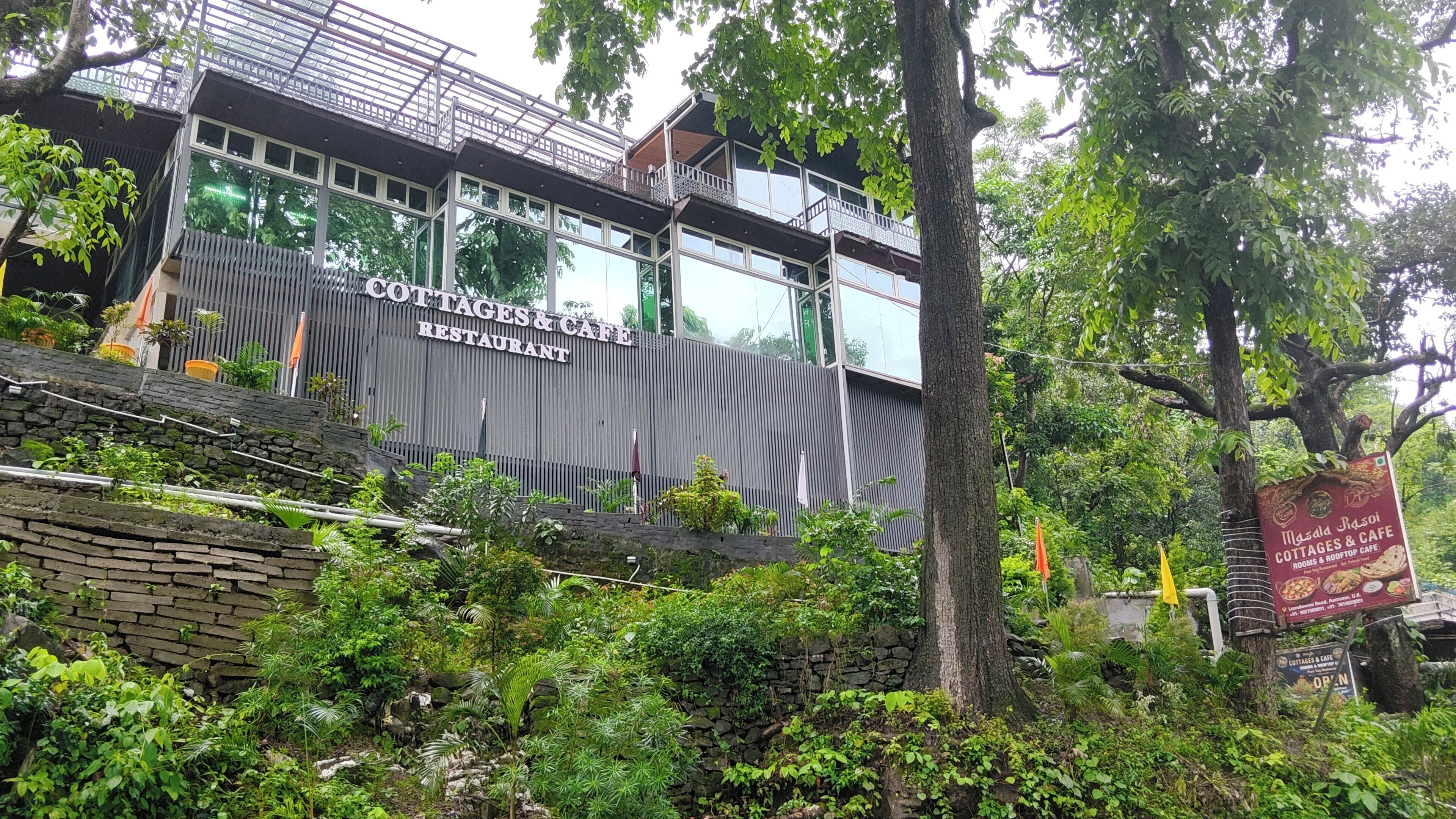 A modern building with a sign for 'Cottages & Cafe Restaurant' featuring a glass facade and a stone base.