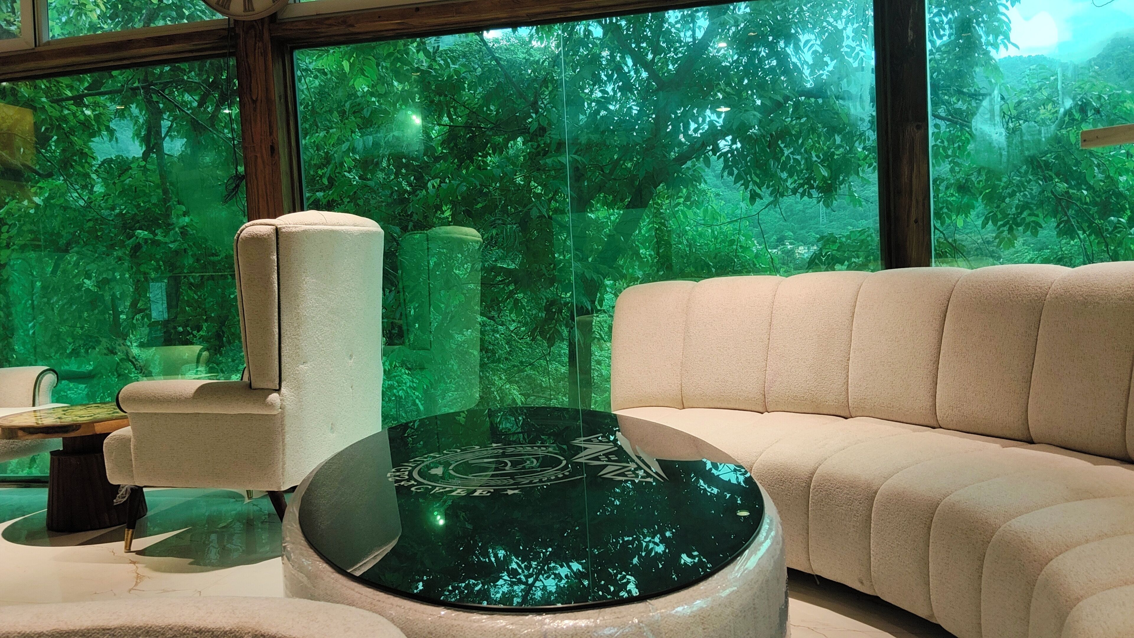 A modern living room with a sofa, armchair, and a glass coffee table with a reflective surface.