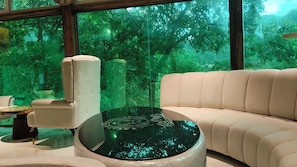 A modern living room with a sofa, armchair, and a glass coffee table with a reflective surface. - Cottages & Cafe (Kotdwar)