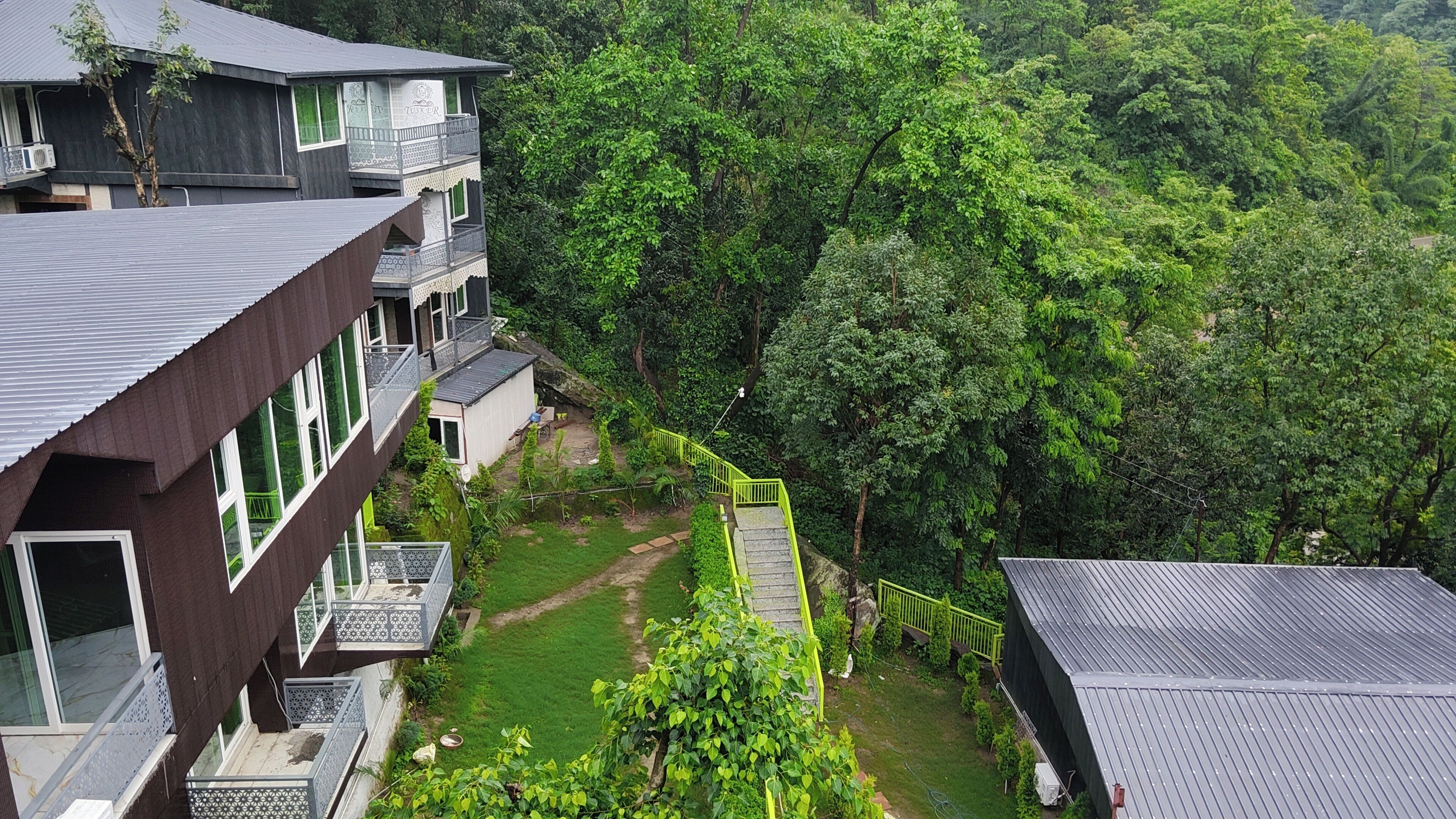 A multi-story building with balconies, surrounded by lush greenery and a clear sky.