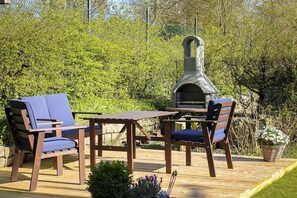 Eine Außenpatio mit einem Holztisch und Stühlen, einem Steingrill und üppigem Grün im Hintergrund.