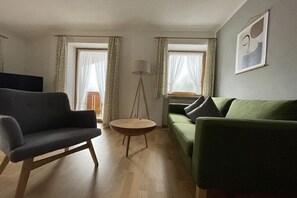 A living room with a dark grey armchair, a green sofa, a round wooden coffee table, and a floor lamp. - "Kehstein" in the "Bartmann" house (Ramsau)