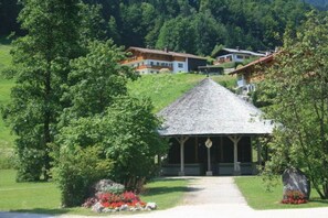 A traditional chalet with a sloped roof, surrounded by lush greenery and a clear path leading to the entrance. - "Kehstein" in the "Bartmann" house (Ramsau)