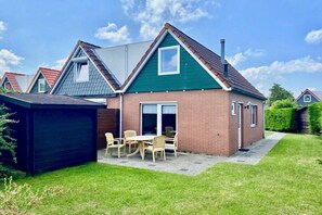 Une maison à deux étages avec une façade en briques, un toit végétalisé et une terrasse aménagée avec du mobilier d’extérieur.