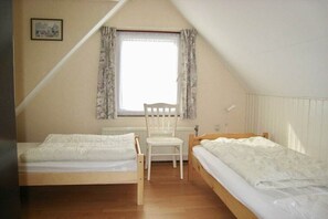 Une chambre avec deux lits, une chaise, une fenêtre avec des rideaux et un radiateur.