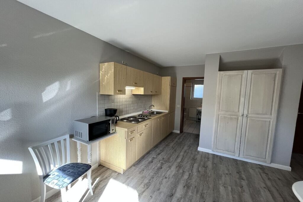 Una cocina con armarios de madera, microondas, fregadero y una silla.