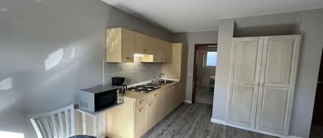 A kitchen with wooden cabinets, a microwave, a sink, and a chair.