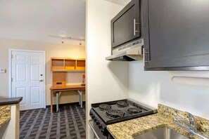 A compact kitchen with a stove, microwave, and granite countertop.