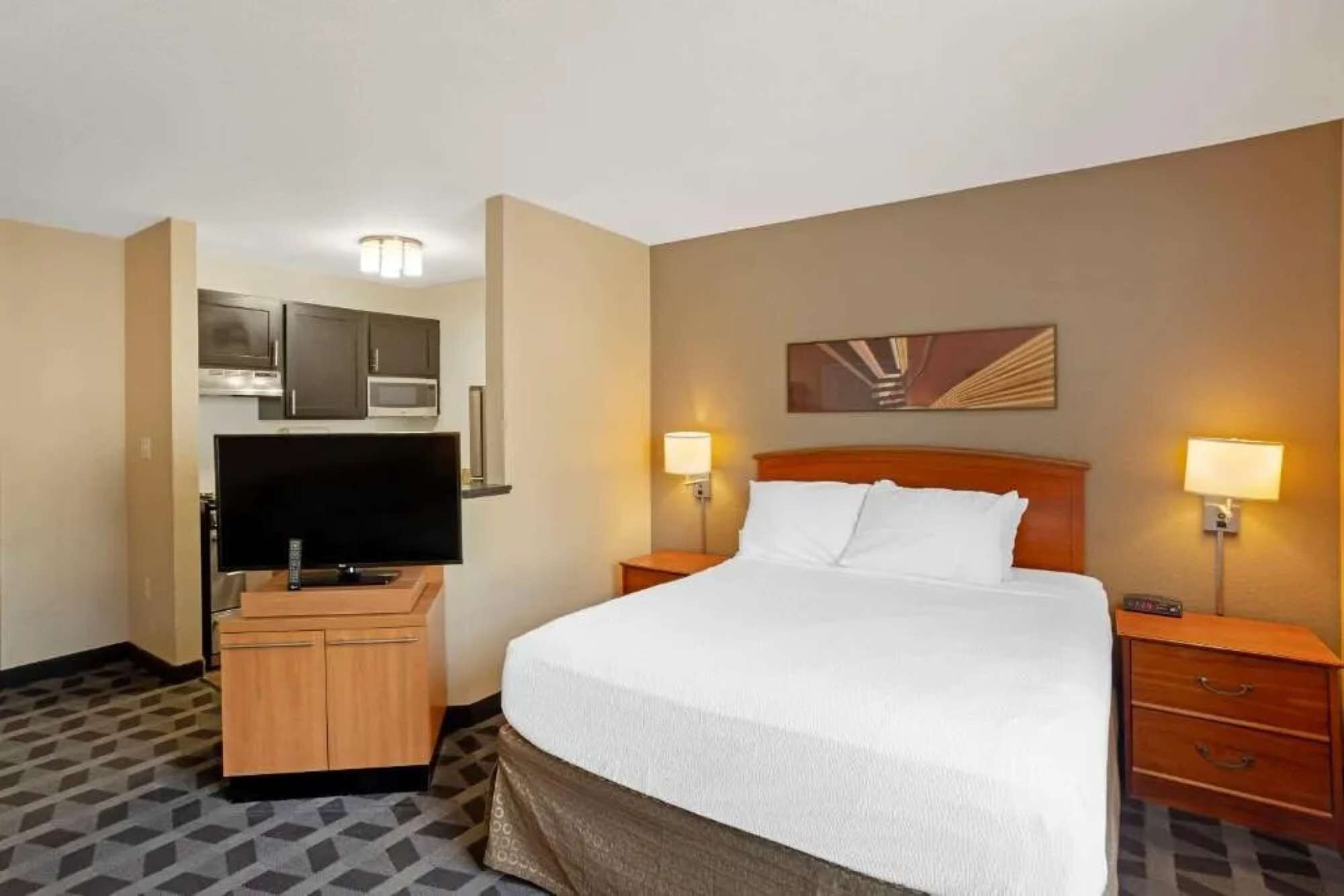 A hotel room with a bed, a television, a desk with a computer, and a microwave.