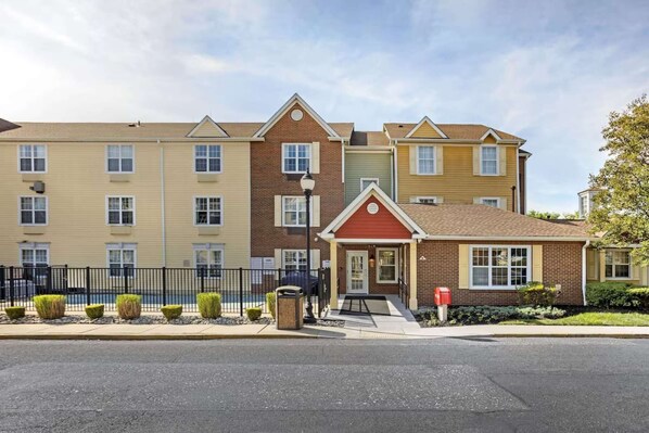 A multi-story residential building with a central entrance, a small attached garage, and a fenced parking area. - Your Home Base Near Philly + Free Parking. Kitchen (Mount Laurel)