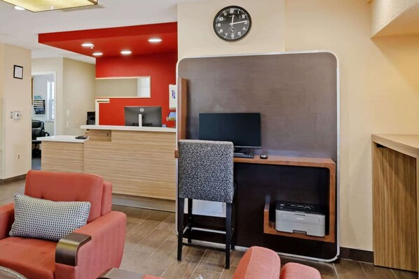 A hotel room with a desk, a television, and a clock on the wall.