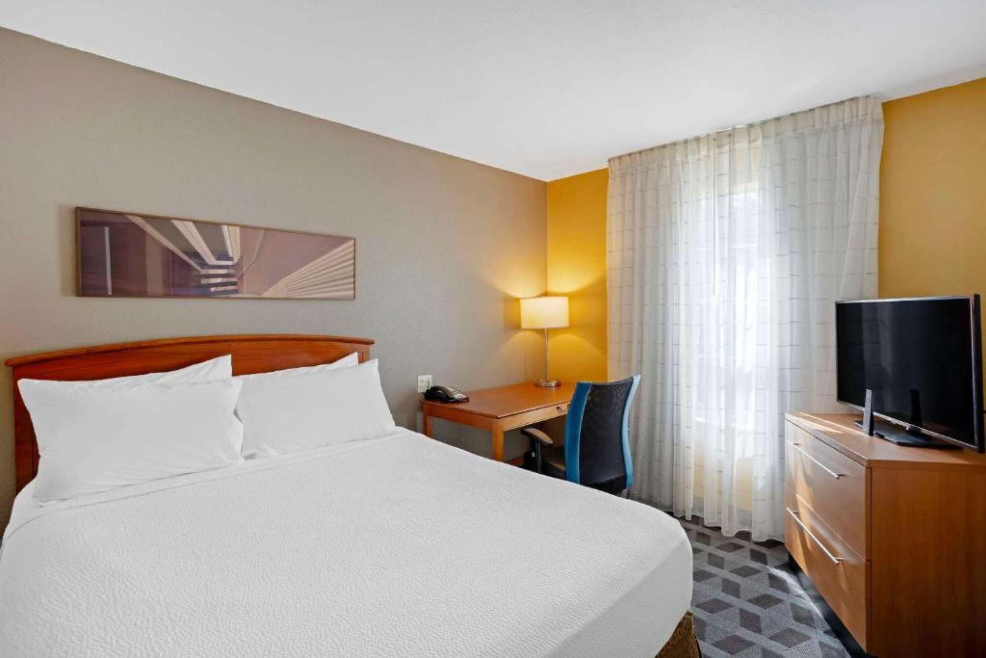 Ein Hotelzimmer mit Bett, Schreibtisch, Stuhl, Fernseher und Lampe.