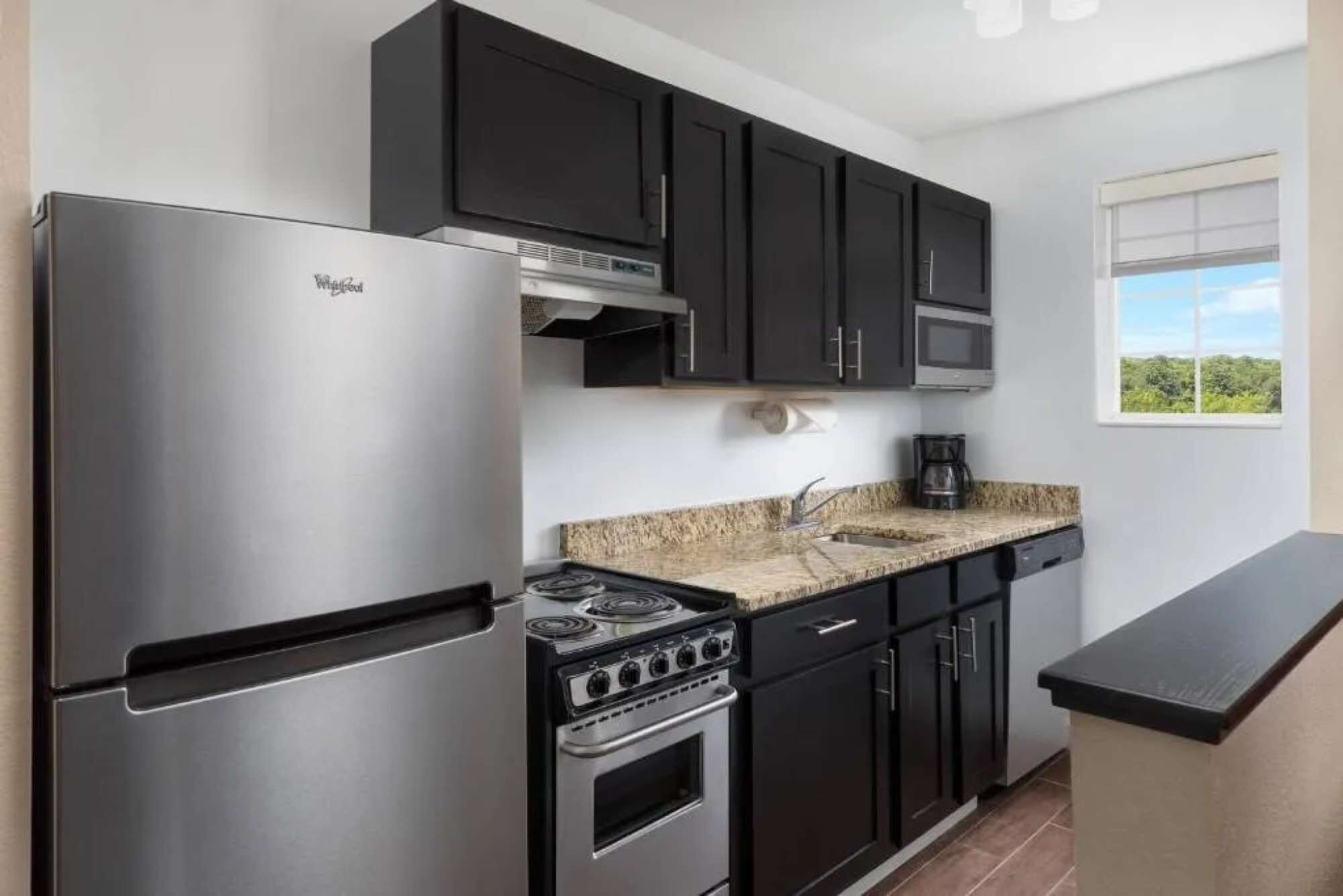 A modern kitchen with a stainless steel refrigerator, a gas stove, and dark cabinetry.