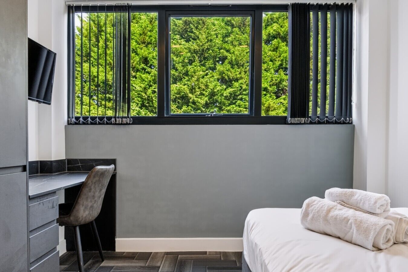A hotel room with a bed, a desk, and a window with curtains.