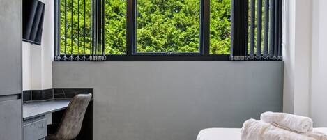 A hotel room with a bed, a desk, and a window with curtains.