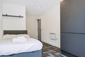 A modern bedroom with a bed, a wall-mounted heater, and a grey wardrobe. - Brand New Spacious Studio in Beeston (Beeston)